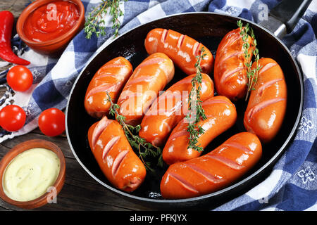 Salati fritti caldi succosa salsicce di manzo con timo fresco sulla padella sul legno scuro tavolo da cucina con peperoncino, ketchup e base di salsa aioli, hor Foto Stock