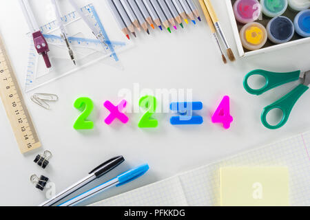 L'equazione matematica "2*2=4' da multi-colore numeri di plastica su uno sfondo bianco con la scuola articoli. Foto Stock