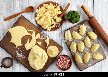 Non cotti pierogi - tradizionale polacco o gnocco ucraino è riempito con purea di patate e il prosciutto tritato finemente o pancetta sul tagliere di legno con Foto Stock