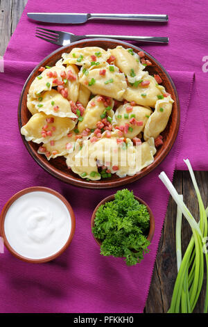 Delizioso caldo gnocchetti fatti in casa con purea di patate e carne ripieno su una piastra di argilla sulla tabella mat servito con panna acida in una ciotola e verdi, vertic Foto Stock