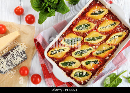 Deliziosa pasta grandi conchiglie al forno farcito con crema di formaggio morbido e spinaci conditi con formaggio parmigiano in una teglia. formaggio parmigiano grattugiato su Foto Stock