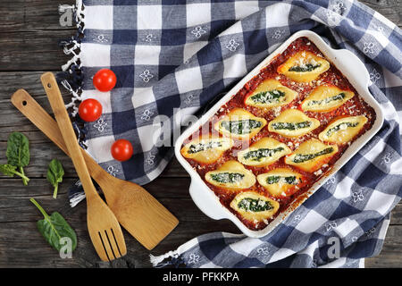 Forma a guscio pasta farcita con crema di formaggio morbido e spinaci conditi con formaggio parmigiano in una teglia con carta asciugatutto e spatole in legno su Foto Stock