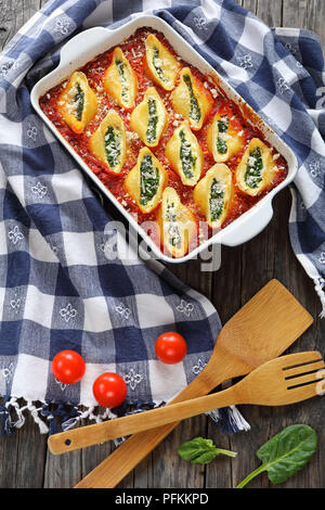 Cotti in forno a forma di guscio di pasta farcita con crema di formaggio morbido e spinaci conditi con formaggio parmigiano in una teglia con carta asciugatutto e woode Foto Stock