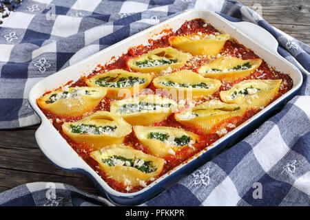Forma a guscio pasta farcita con crema di formaggio morbido e spinaci cotti in forno, cosparso con parmigiano grattugiato in una teglia con carta asciugatutto Foto Stock