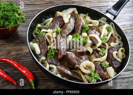 Close-up di deliziosi piatti ben cotti di fegato di vitello pezzi fritti con scalogno e anelli in padella, vista da sopra Foto Stock