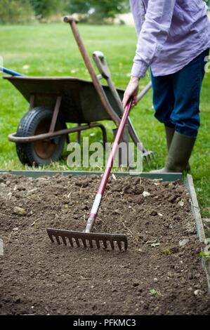 La rastrellatura il terreno in un orto, carriola, a Forcella e forcella in background Foto Stock