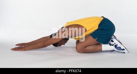 Giovane uomo di eseguire la parte inferiore della schiena esercizio di stiramento, inginocchiata sul terreno, braccia davanti a lui, vista laterale Foto Stock