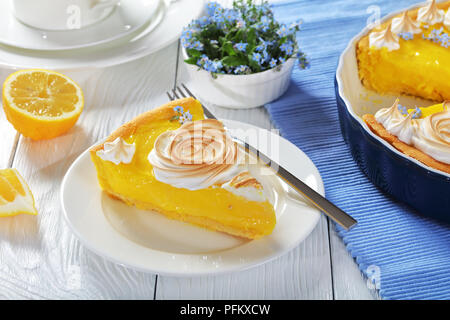 Fetta di francese classica crostata al limone - pasta croccante con un uniforme riempimento di limone decorato con rose di meringa e commestibile fiori freschi, close-up Foto Stock