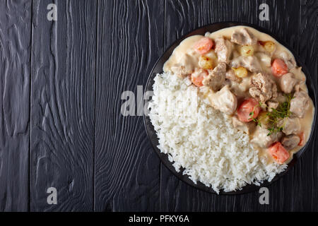 Blanquette di vitello - pezzi di carne, funghi, cipolline, erbe,Verdure con salsa cremosa servito con riso su una piastra nera sul tavolo di legno, fr Foto Stock