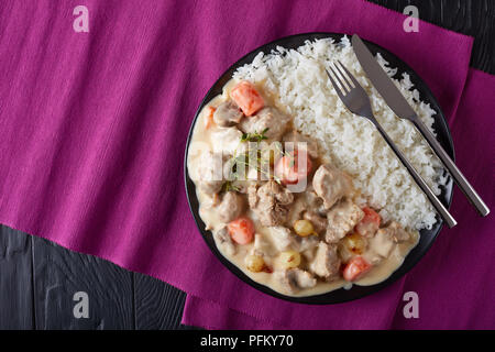 Blanquette di vitello - pezzi di carne, funghi, cipolline, erbe,Verdure con salsa cremosa servito con riso su una piastra nera sul tavolo di legno, fr Foto Stock