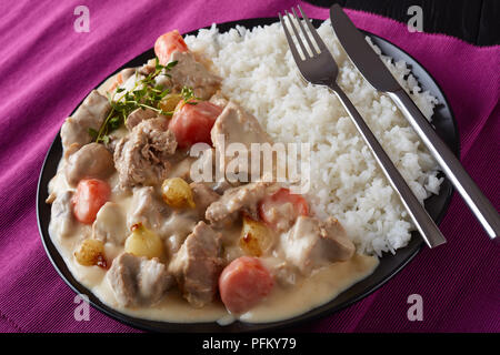 Blanquette di vitello - pezzi di carne, funghi, cipolline, erbe,Verdure con salsa cremosa servito con riso su una piastra nera sul tavolo di legno, fr Foto Stock