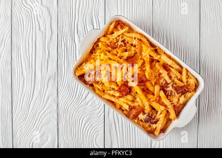 Croccanti patatine fritte soffocato nel formaggio fuso e il bacon in una teglia su una tavola di legno, vista da sopra, laici piatta Foto Stock