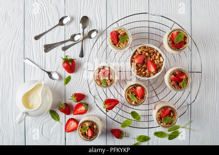 Deliziosa casa granola stratificata con yogurt fresco e fragole mature nella porzione di vasi in vetro sulla griglia metallica, vista orizzontale dal di sopra, Foto Stock