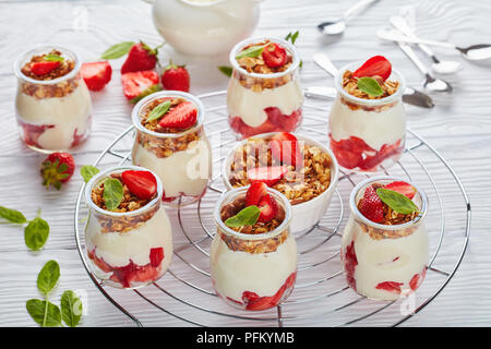 Deliziosa casa granola stratificata con yogurt fresco e fragole mature nella porzione di vasi in vetro sulla griglia metallica, vista orizzontale dal di sopra, close-up Foto Stock