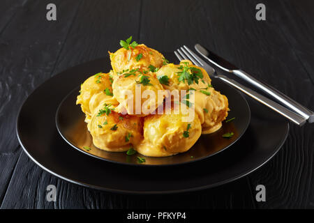 Nuovo delizioso di patate con formaggio fuso con il prezzemolo tritato servito sulla piastra nera con argento forchetta e coltello su un di legno nero, tabella vi Foto Stock