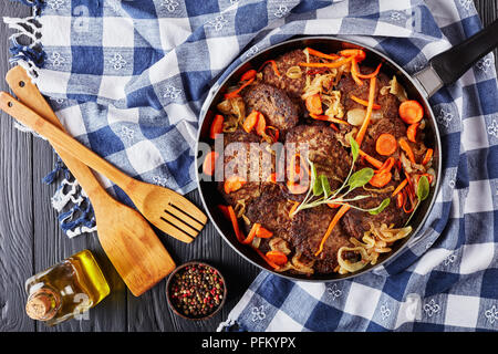 Deliziosa di fegato di pollo frittelle con la carota, la cipolla, le erbe aromatiche e le spezie in una padella con carta asciugatutto e spatole in legno sulla tavola nera, vista da ab Foto Stock