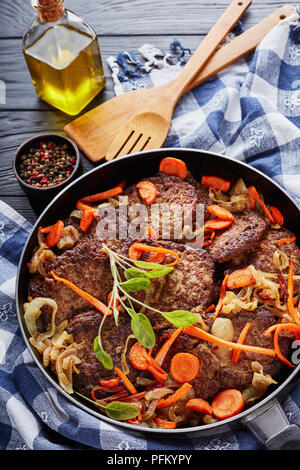 Fegato di pollo frittelle con la carota, la cipolla, le foglie di salvia e spezie in una padella su tavoli in legno nero con carta asciugatutto e spatole in backgrou Foto Stock