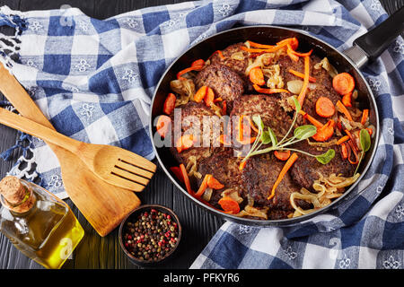 Fegato di pollo frittelle con la carota, la cipolla, le foglie di salvia e spezie in una padella su tavoli in legno nero con carta asciugatutto e spatole in backgrou Foto Stock