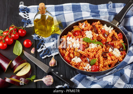 Vegetariano Pasta italiana fusilli alla Norma con melanzane, pomodori e basilico, ricotta e salsa marinara in una padella con ingredienti a bac Foto Stock