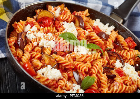 Vegetariano Pasta italiana fusilli alla Norma con melanzane, pomodori e basilico, ricotta in una padella su di un tavolo di legno, vista da sopra, close-up Foto Stock