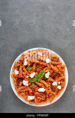 La pasta italiana I fusilli alla Norma con melanzane, pomodori e basilico, ricotta in una piastra bianca su una tavola di cemento, vista da sopra, laici piatta Foto Stock