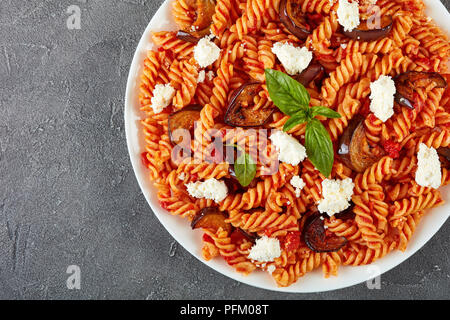 La pasta italiana I fusilli alla Norma con melanzane, pomodori e basilico, ricotta in una piastra bianca su una tavola di cemento, vista orizzontale dal di sopra, piatto Foto Stock