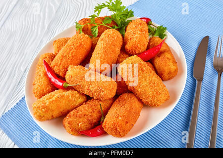 Close-up di spagnolo fritte dorate crocchette di patate, croquetas su una piastra bianca su una tavola di legno con coltello e forchetta, vista da sopra Foto Stock