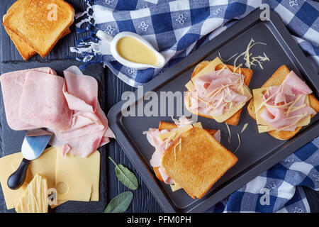 French Toast croque monsieur preparato per cuocere. burro tostato pane con fette di prosciutto bollito e formaggi Emmental su una teglia da forno con ingredienti o Foto Stock