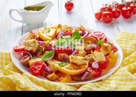 Freschi e deliziosi italiano insalata estiva panzanella con pomodori, crostini e anelli di cipolla su una piastra bianca su una tavola di legno con salsa di olio di oliva a Foto Stock