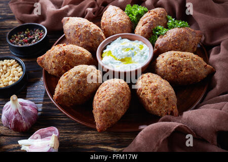 Fritte kibbeh di macinato di carni bovine miscelate con bulgur, farcite con fritto di carne macinata con pinoli, spezie, aglio ed erbe aromatiche su una piastra di argilla su un Foto Stock
