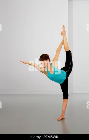 La donna nella parte superiore blu e nero leggings eseguire esercizi di allungamento, in piedi su una gamba sola, altra gamba dritta fino, braccia in alto Foto Stock