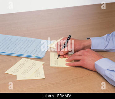 Man mano scheda scrittura richiede, accanto alla pila di appunti scritti a mano su carta blu, close-up Foto Stock