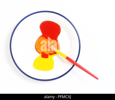 La miscelazione di colore rosso e giallo vernice su una piastra utilizzando un pennello piccolo, vista da sopra Foto Stock