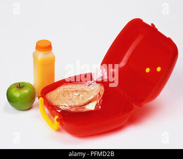 Pitta sandwich di pane in open red lunchbox, bottiglia di succo di arancia e mela verde sul lato. Foto Stock