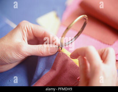 Le mani di metallo di cucitura degli anelli della tenda al rosso, blu e giallo materiale, tirando, filato da ricamo attraverso gli anelli di occhiello. Foto Stock