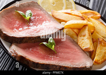 Bistecca di manzo è servito con patate arrosto e limone close-up su una piastra su una tavola nera orizzontale. Foto Stock