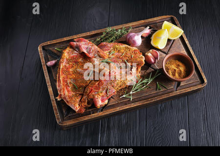 Close-up di crudo fresco di ricambio costolette di agnello marinato per essere cotto con rosmarino, timo, mix di spezie di terra, aglio e le fette di limone su rustico in legno cutt Foto Stock