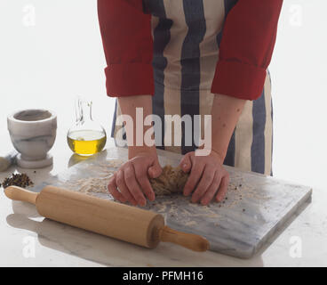 Impastare la pasta la pasta su una scheda in marmo accanto a un matterello, un vasetto di olio di oliva e un pestello e mortaio. Foto Stock