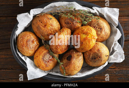 Close-up di pane appena sfornato patate intere con il timo in una teglia sul tavolo di legno, orizzontale vista da sopra Foto Stock