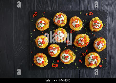 Patate cotte due volte metà caricato con formaggio Cheddar grattugiato, pancetta, peperoncino fette, panna acida fresca e cosparsi di cipolla verde sulla stecca Foto Stock