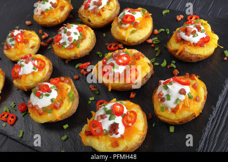 Close-up di due volte di patate al forno metà caricato con formaggio Cheddar grattugiato, pancetta, peperoncino fette, panna acida e cosparsi di cipolla verde su SLA Foto Stock