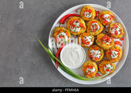 Deliziose patate al forno metà caricato con formaggio Cheddar grattugiato, pancetta, peperoncino fette, panna acida sulla piastra bianca su sfondo di calcestruzzo, vista Foto Stock