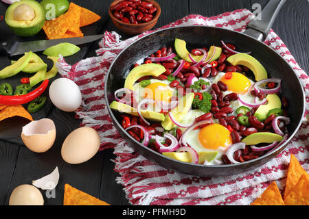 Close-up di una deliziosa colazione messicana - uova fritte, fagioli rossi, fette di avocado , anelli di cipolla, peperoncino jalapeno e peperoni in padella, ingredienti Foto Stock