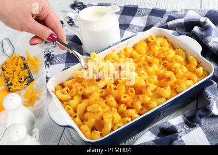 Donna di mano è in possesso di una forcella con una piccola porzione di Mac e formaggio o il gomito pasta al forno con panna e formaggio Cheddar forte in salsa di piatto, autentica Foto Stock
