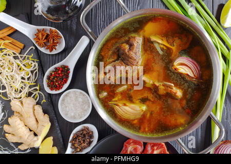 Carni bovine il brodo di osso e altri ingredienti per la classica zuppa vietnamita Pho Bo, con carne di manzo crudo, germogli di soia, scalogni cotti al forno, riso, pasta, salsa di pesce, spezie, Foto Stock