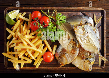 Deliziosa freddo affumicato luna pesce e patatine fritte servite su marrone tagliere su tavola in legno rustico, vista da sopra, close-up Foto Stock