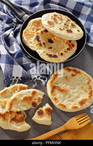 Fritti di fresco pane pita in padella con carta asciugatutto e spatole in legno su cemento Tabella, vista verticale da sopra Foto Stock