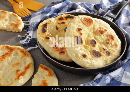 Close-up di fritto di fresco pane pita in padella con carta asciugatutto e spatole in legno su cemento Tabella, vista orizzontale dal di sopra Foto Stock