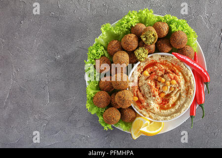 Deliziosa fritte palline di falafel con hummus in una ciotola, peperoncino e foglie di lattuga su piastra su calcestruzzo sfondo, vista orizzontale dal di sopra Foto Stock