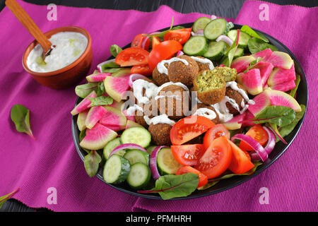 Gustosa falafel sfere con lo yogurt greco in salsa di piastra con verdure insalata colorata di anguria ravanello, foglie di bietole, cetriolo e fette di pomodoro. tza Foto Stock